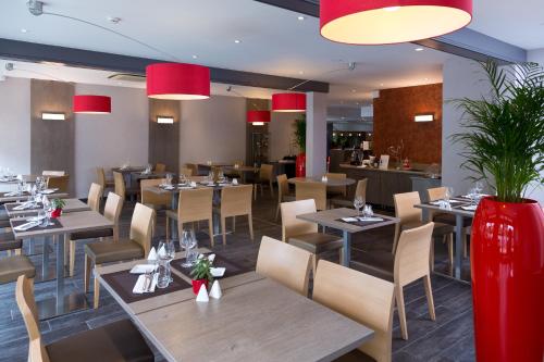 a restaurant with wooden tables and chairs and red lamps at Mercure Strasbourg Aéroport in Ostwald