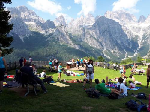 a group of people sitting on the grass in the mountains at Rifugio La Montanara in Molveno