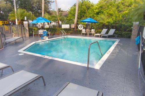 a swimming pool with chairs and umbrellas on a patio at Holiday Inn Express and Suites Fort Lauderdale Airport West, an IHG Hotel in Davie