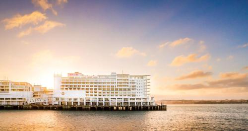 a large white building on the water with the sunset at Hilton Auckland in Auckland
