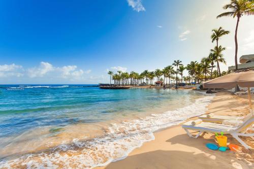 a beach with chairs and palm trees and the ocean at Caribe Hilton in San Juan