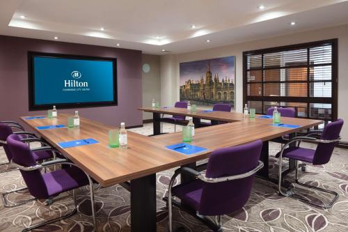 a conference room with tables and purple chairs and a flat screen tv at Hilton Cambridge City Centre in Cambridge