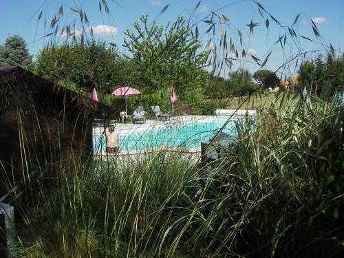 une femme debout au bord d'une piscine avec un parasol rose dans l'établissement Les 4 Saisons, à Sarlat-la-Canéda