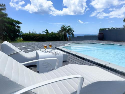 a swimming pool with white chairs and a table at Villa Jouanacaera in Le Carbet