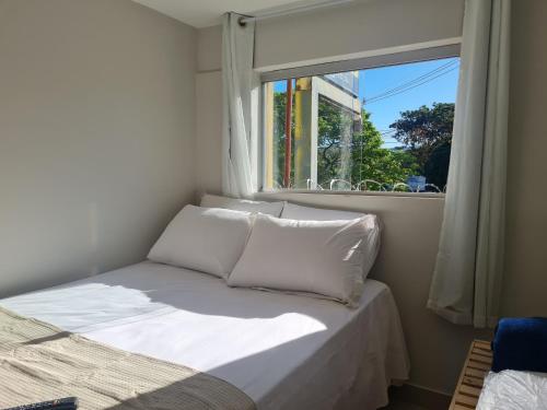uma cama com almofadas brancas num quarto com uma janela em Apt 17 com 2 suítes com ar cond em Montes Claros