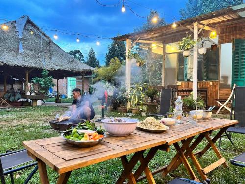 un hombre cocinando comida en una mesa de madera en un patio trasero en Nhà nghỉ đèo Tà Pứa 