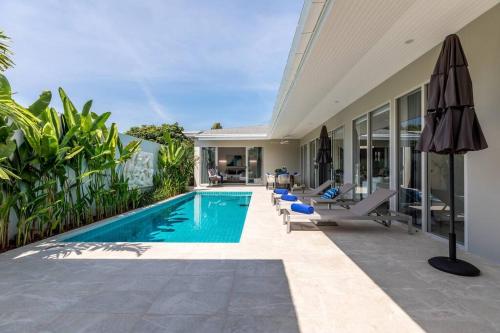 a swimming pool with chairs and an umbrella next to a house at Big & Stylish 5 Bed 4 Bath Private Garden Pool Villa at Thongson Bay Beach in Koh Samui 