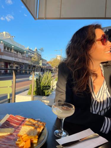 a woman sitting at a table with a glass of wine at Little Lane Apartments Comfortable, Chic New Apartment in Heart Of Fremantle Features Large balcony & Free car bay in Fremantle