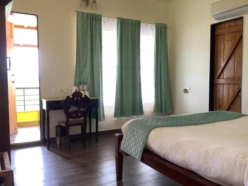 a bedroom with a bed and a desk and green curtains at Vallonne Vineyards in Igatpuri