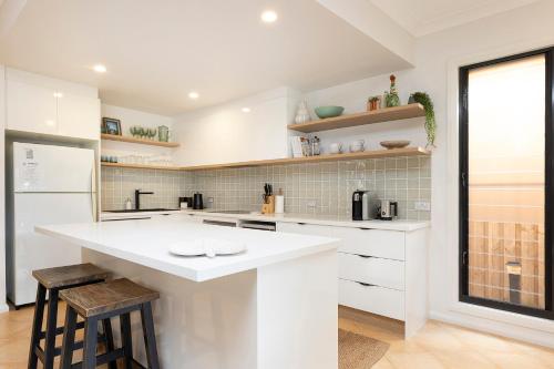 a white kitchen with a large white counter and stools at Gwydir Court 1 in Forster