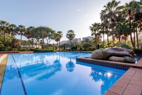 a swimming pool with a large rock and palm trees at Club Wyndham Coffs Harbour Terraces in Coffs Harbour