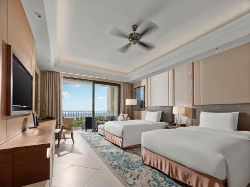 a hotel room with two beds and a flat screen tv at Hilton Haikou Meilan - Beachfront Hotel in Haikou