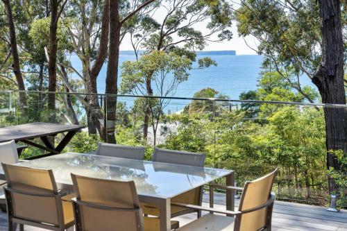 a table and chairs on a balcony with a view of the ocean at Treehaven Hyams Beach in Hyams Beach