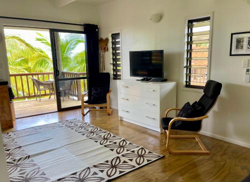 a living room with a television and a dresser and chairs at Rarotonga Villas Absolute Beachfront in Arorangi