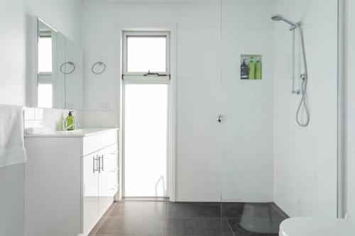 a white bathroom with a shower and a sink at Derwent River Cottage - Tranquil Waterfront Living in Goodwood