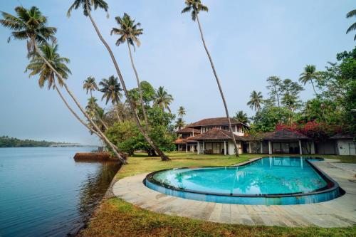 a house with a swimming pool next to a body of water at Cranganor History Café & Riverside Château in Parūr