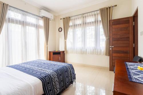 a bedroom with a bed and a desk and windows at Jenna Residence Denpasar in Denpasar