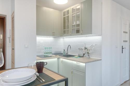 a white kitchen with white cabinets and a table at Olive City View Apartment in Wrocław
