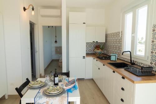 a kitchen with white cabinets and a table and a sink at Vela Bianca Marzamemi in Marzamemi