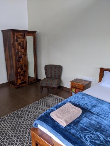 a bedroom with a bed with a blue blanket and a chair at Moksha at Infinity Valley in Kotagiri