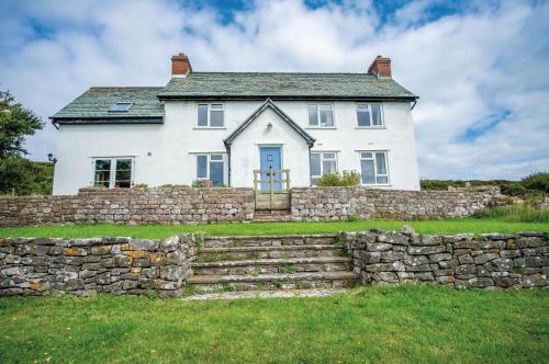 a white house behind a stone wall at Windy Walls - 3 Bedroom Holiday Home - Rhossili in Rhossili
