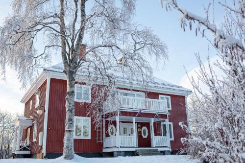 uma casa vermelha com uma árvore na neve em Jokkmokks Vandrarhem Åsgård em Jokkmokk