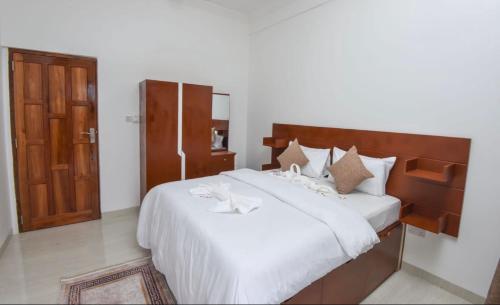 a bedroom with a bed with white sheets and a wooden door at JOY B Apartment 2 in Kiembi Samaki