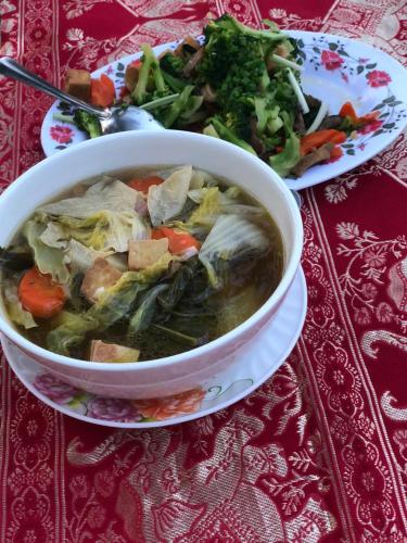 a bowl of soup on a table with a plate of food at Bloom Garden Bed & Breakfast in Siem Reap