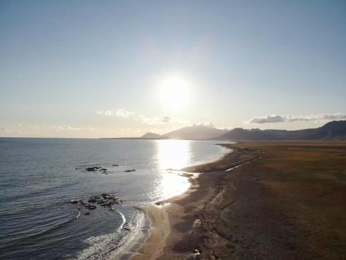 a beach with the sun shining on the water at Vatnsholt in Snæfellsnes - Birta Rentals in Snæfellsbær