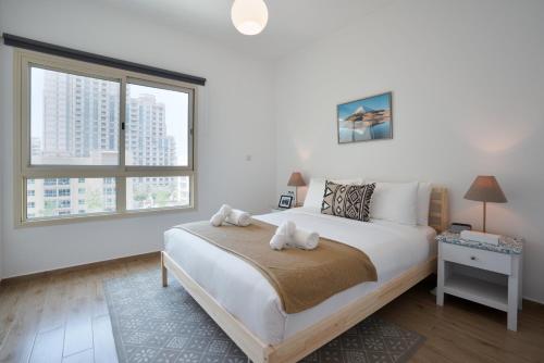 een witte slaapkamer met een groot bed en 2 ramen bij Luxurious Apt with Balcony The greens Dubai in Dubai