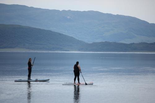 two people are standing on paddle boards in the water at Clovullin Croftview Pod in Ardgour