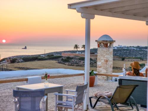 a woman sitting in chairs on the beach at sunset at Anthemion Paros - Villas & Suites in Agia Irini Paros