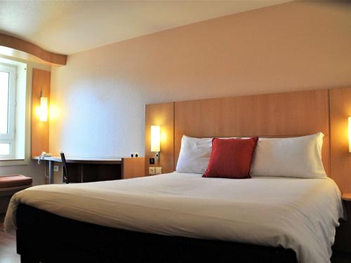a hotel room with a large bed with a red pillow at ibis Toulouse Centre in Toulouse
