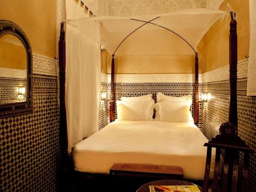 1 dormitorio con cama con dosel, sábanas y almohadas blancas en Riad ka en Marrakech
