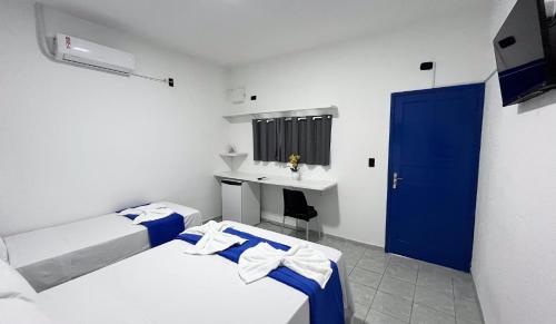 two beds in a room with a sink and a blue door at Pousada Estação do Porto in Porto De Galinhas