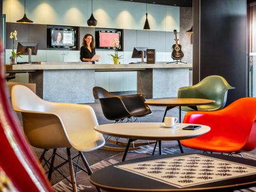 a bar with colorful chairs and a woman sitting at a counter at Ibis Marne la Vallée Noisy in Noisy-le-Grand