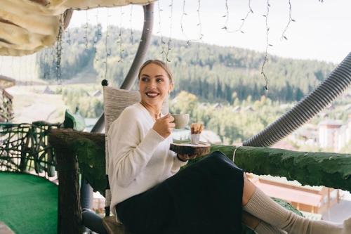 a woman sitting on a swing with a cup of coffee at Грибова хата in Bukovel