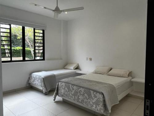 a white bedroom with two beds and a window at Monte Escondido-Condominio Campestres Altos de Komulá - Anapoima in Anapoima