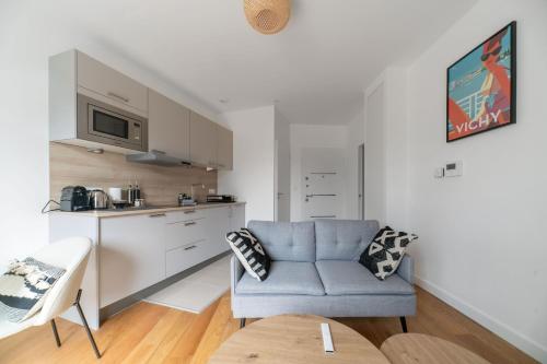a living room with a blue chair and a kitchen at Le Royal - Appartement design - Hyper centre in Vichy