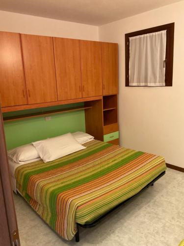 a bedroom with a bed with a green headboard and wooden cabinets at RESORT VILLAGE AQUA MARINA FAMILY - Daily Rooms Tidying - CocktailsBar- Pet Friendly - with Hypermarket - Delivery Restaurant-Pizzeria - Room Breakfast with supplement - Ultra Fast Wi-Fi - Play Area for children - Olympic Swimming Pool - Parking in Caorle