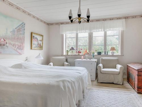 a white bedroom with a bed and a chair and windows at Holiday Home Arvidstorp by Interhome in Johannishus