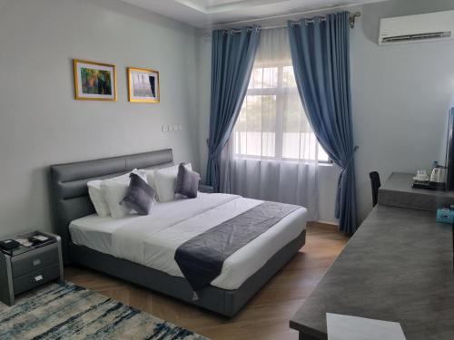 a bedroom with a bed with blue curtains and a window at Solace Suites and Homes Maiduguri in Maiduguri