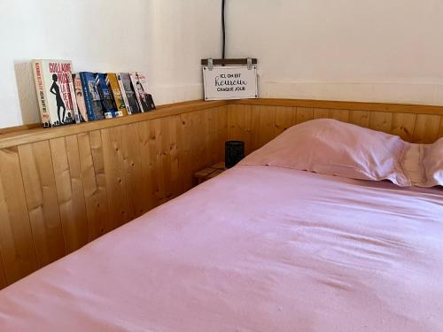 ein Bett mit einer rosa Decke und Büchern auf einem Regal in der Unterkunft Le poulailler 