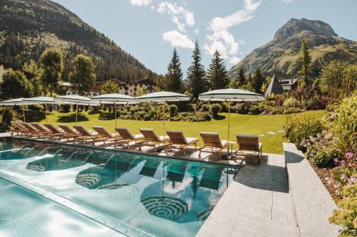 a swimming pool with chairs and a mountain at Hotel Arlberg Lech in Lech am Arlberg