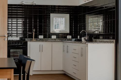 una cocina con armarios blancos y una pared de azulejos negros en Casa Amancay en San Carlos de Bariloche