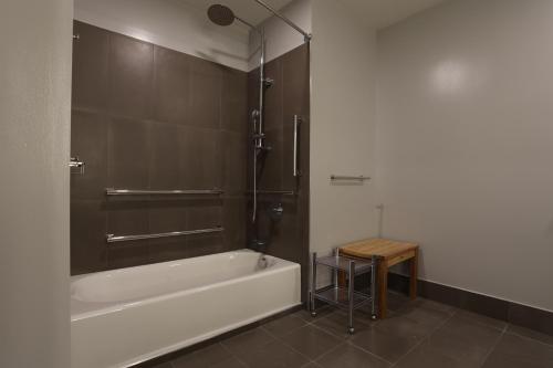 La salle de bains est pourvue d'une baignoire, d'une douche et d'un tabouret. dans l'établissement Cedartree Hotel Portland Hillsboro, à Hillsboro