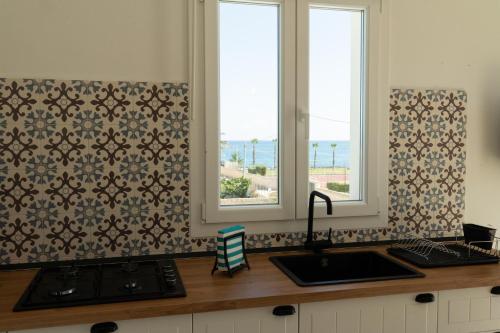 a kitchen with two windows and a counter with a sink at Vela Bianca Marzamemi in Marzamemi