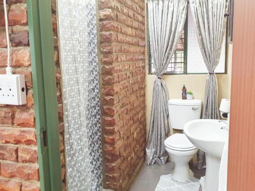 a bathroom with a white toilet and a brick wall at Garden cottages near Savannah Mall in Polokwane