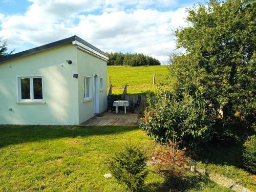une petite maison blanche dans un champ avec une terrasse en bois dans l'établissement La petite maison au calme dans les champs, à Matton-et-Clémency