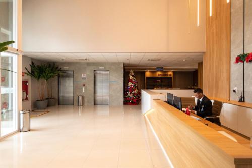 a man sitting at a desk in a lobby with a christmas tree at Studios aconchegantes no Setor Marista BLS in Goiânia